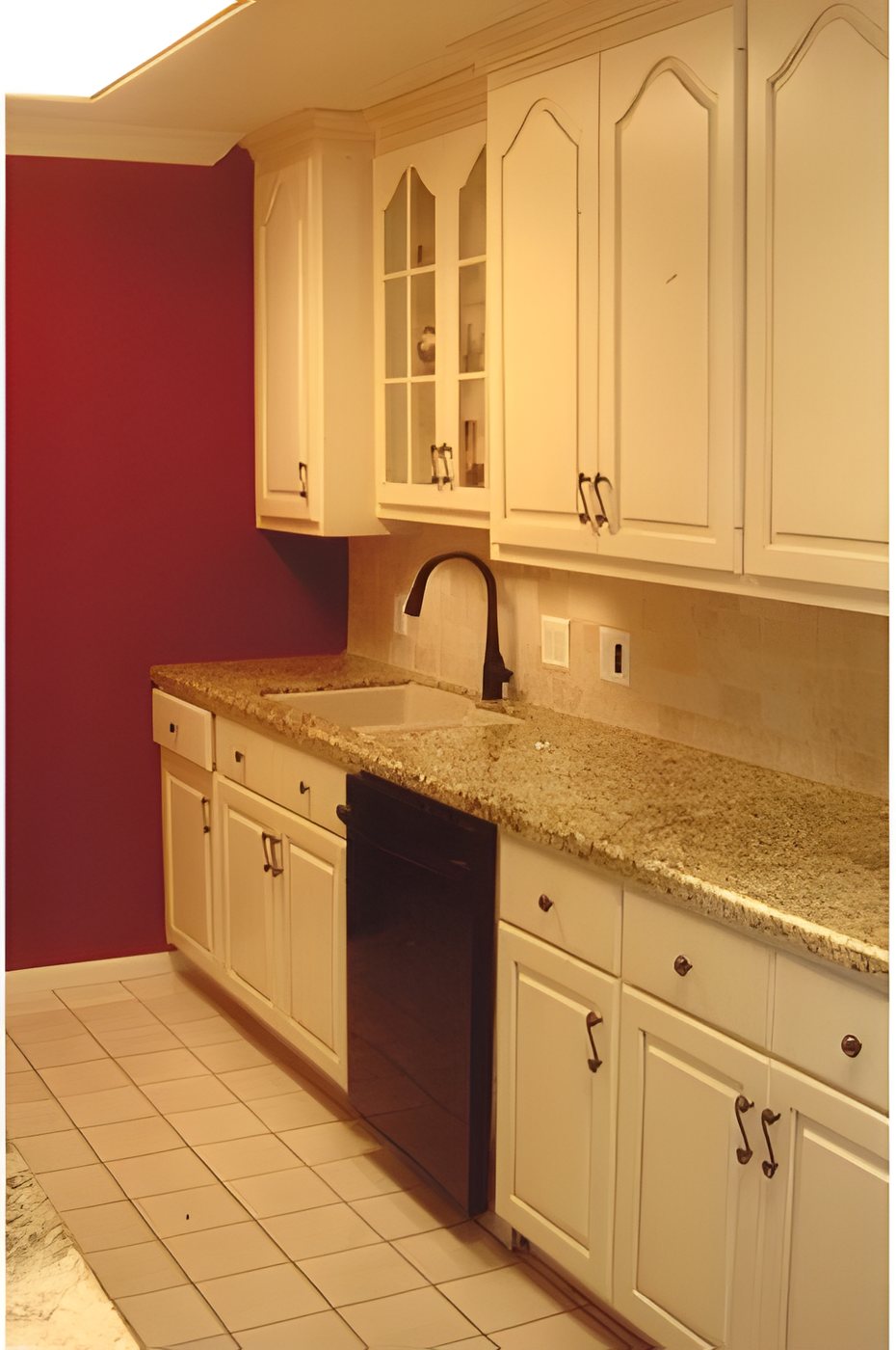 Kitchen with cream cabinets, arched upper doors, granite counters and a red accent wall